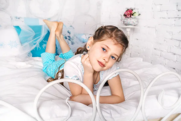 美しい小さな女の子は彼女の寝室で白い毛布の上に座っています。 — ストック写真