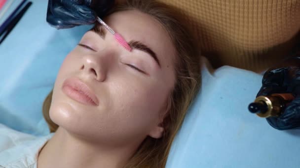 Master makes permanent eyebrow makeup procedure using special needle tattoo machine to woman in beauty salon. Microblading brows tattooing. Dark pigment is injected under skin. Cosmetology procedure — Vídeo de Stock