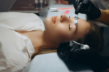 Ustabaşının ellerinde fırçayı tutarken usta, kaşların dökülmesinden sonra saçların uzamasını yönetir.