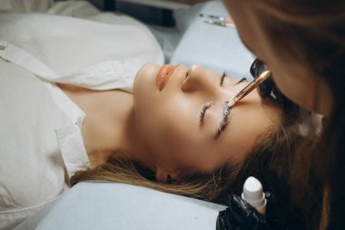 Ustabaşının ellerinde fırçayı tutarken usta, kaşların dökülmesinden sonra saçların uzamasını yönetir.