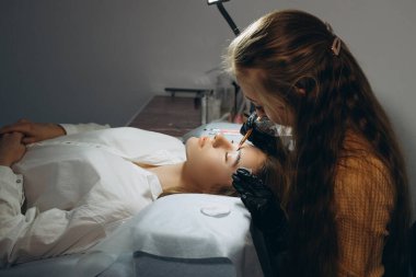 Ustabaşının ellerinde fırçayı tutarken usta, kaşların dökülmesinden sonra saçların uzamasını yönetir.