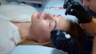 Ustabaşının ellerinde fırçayı tutarken usta, kaşların dökülmesinden sonra saçların uzamasını yönetir.