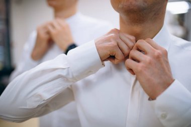 Beyaz gömleğin arka planında erkek elleri kol düğmeleri ve saatlerle kol gömleği, yakın plan çekimleri.