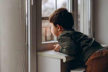 Küçük, düşünceli, iki yaşında bir çocuk pencerenin kenarında oturup oyuncak çocuk arabasıyla oynuyor.. 