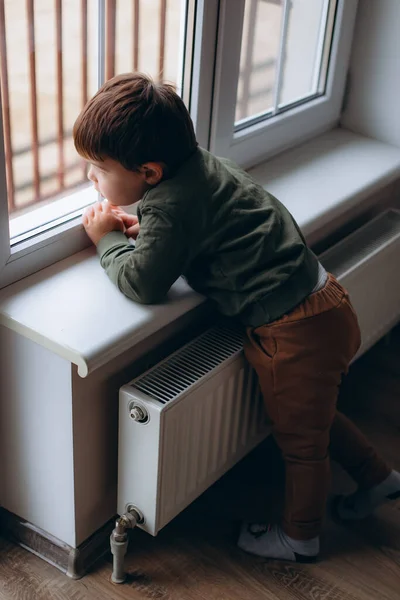 Kicsi, töprengő, két éves fiú ül az ablaknál, és játékautóval játszik. — Stock Fotó
