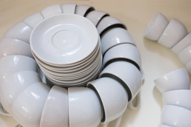 Beyaz arka planda, şeffaf şarap kadehleriyle ahşap bir masaya istiflenmiş beyaz bulaşık takımı..