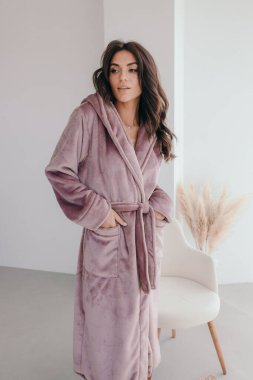 Beyaz bornozlu bir kızın büyük pencereli bir odada küvetin yanında durduğunu hayal et. Yüksek kalite fotoğraf