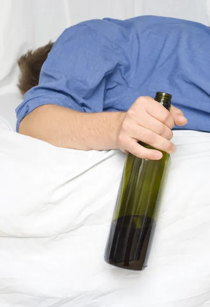 O homem desmaiou na cama com uma garrafa de vinho. — Fotografia de Stock
