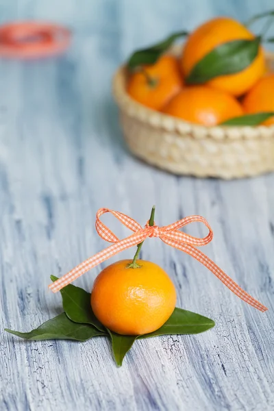 Un mandarin contre le panier. Placé sur les feuilles. Rouleau de ruban adhésif sur le fond — Photo