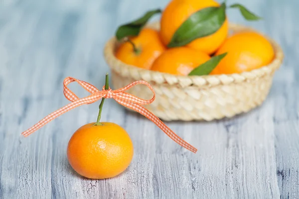 Jedna mandarinka s barevnými pásky luk uzel. některé mandarinky v košíku na pozadí — Stock fotografie