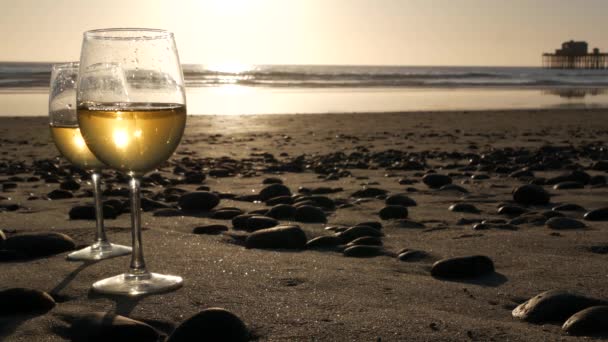 Två vinglas på havsstranden. Glasögon med vitt vin för romantisk dejt, havsvatten. Solnedgångsvågor. — Stockvideo