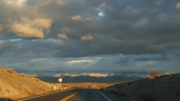 Viaggio in auto dalla Death Valley a Las Vegas, Nevada, USA. Autostop in viaggio in America. Viaggio in autostrada, atmosfera drammatica, montagna al tramonto e deserto del Mojave. Vista dalla macchina — Foto Stock