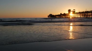 Günbatımında iskele silueti, California USA, Oceanside. Sörf merkezi, okyanus tropik plajı. Dalgayı bekleyen sörfçü.