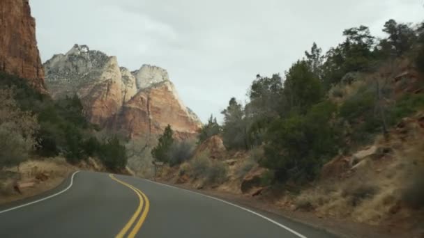 Viaje por carretera, conducción de automóviles en Zion Canyon, Utah, EE.UU. Autoestop viajando por América, viaje de otoño. Acantilados escarpados alienígenas rojos, lluvia y árboles desnudos. Clima brumoso y ambiente tranquilo de otoño. Vista desde el coche — Vídeo de stock