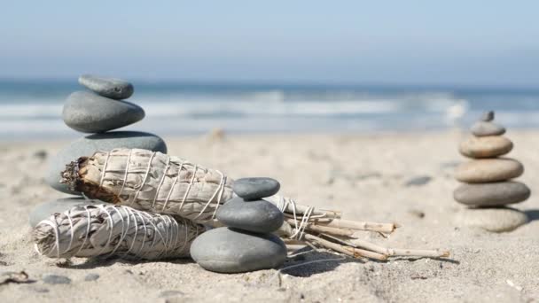 Rock balance on ocean beach, stones stack by sea water waves. Pyramid of pebbles, sage smudge stick. — Stock Video