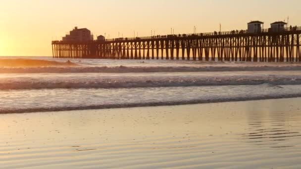 Holzpier auf Pfählen, Silhouette bei Sonnenuntergang, Kalifornien USA, Oceanside. Sonnige Meereswellen bei Sonnenuntergang. — Stockvideo