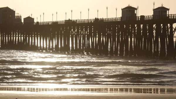 Muelle de madera sobre pilotes, silueta al atardecer, California USA, Oceanside. Olas soleadas al atardecer. — Foto de Stock
