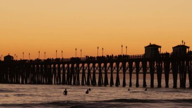 Günbatımında iskele silueti, California USA, Oceanside. Sörf merkezi, okyanus tropik plajı. Dalgayı bekleyen sörfçü.
