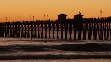 Günbatımında iskele silueti, California USA, Oceanside. Sörf merkezi, okyanus tropik plajı. Dalgayı bekleyen sörfçü.