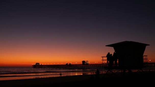 Young teen girls silhouettes, lifeguard watch tower, friends on pacific ocean beach, California USA. — Stock Video