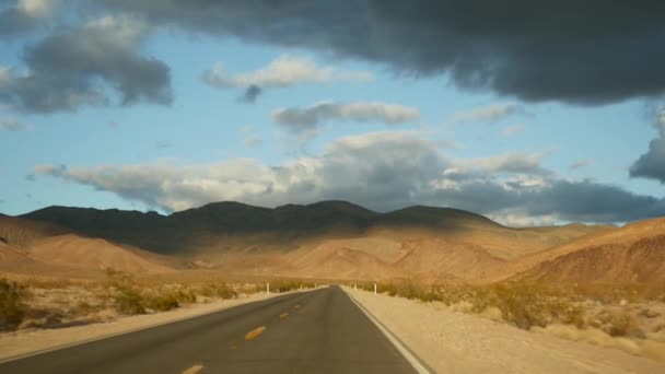 开车从死谷到美国内华达州拉斯维加斯的公路旅行。搭便车在美国旅行。公路旅行，戏剧性的气氛，日落山和莫哈韦沙漠荒原。从车上看 — 图库视频影像