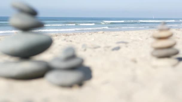 Камень балансирует на берегу океана, камни укладываются морскими волнами. Пирамида гальки на песчаном берегу — стоковое видео