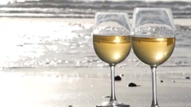 Okyanus sahilinde iki şarap bardağı. Romantik randevu için beyaz şarap bardakları, deniz suyu. Gün batımı dalgaları.