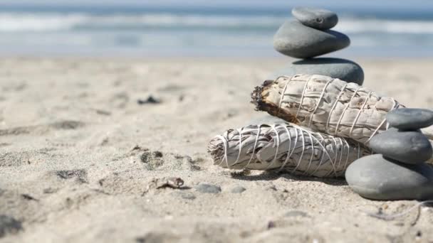 Rock balance on ocean beach, stones stack by sea water waves. Pyramid of pebbles, sage smudge stick. — Stock Video