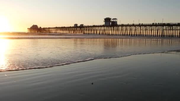 Wooden pier on piles, silhouette at sunset, California USA, Oceanside. Sunny sea waves at sundown. — Stock Video
