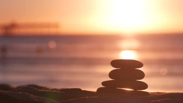 Stack of pebble stones, sandy ocean beach, sunset sky. Rock balancing by water. — Stock Video