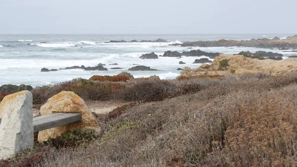 Côte océanique escarpée rocheuse, vagues de mer, Monterey Californie. Banc vide en bois. — Photo