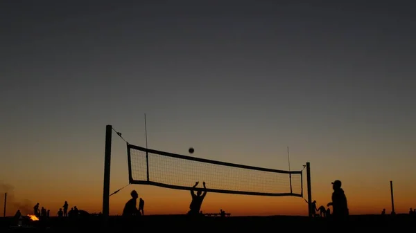 Silueta de red de voleibol en cancha de playa al atardecer, jugadores en la costa de California. —  Fotos de Stock