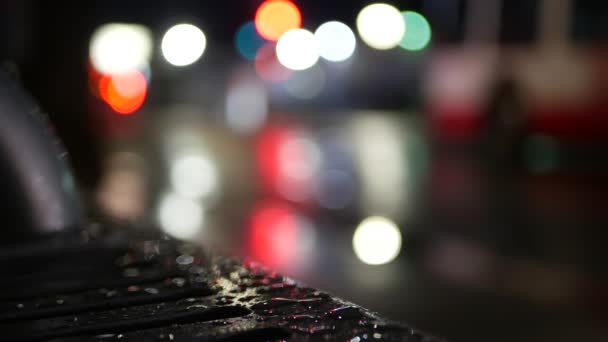 버스 정류장 벤치에는 자동차 교통 신호등 이 반사되어 있습니다. 젖은 금속 위에 물방울이 떨어진다. — 비디오