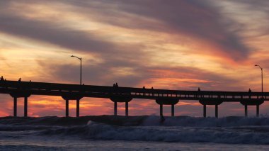 İskelede sörf yapan sörfçüler. Okyanus su dalgaları, insanlar ve gökyüzü gün batımında. Kaliforniya