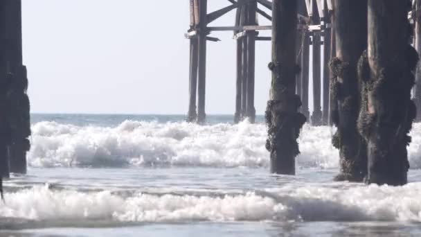 Debajo del muelle de cristal de madera en pilas, olas de agua de la playa del océano, California EE.UU.. — Vídeo de stock