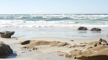 Büyük okyanus dalgası Kaliforniya sahillerine çarpıyor, aşınmış taş ya da kumda kaya.