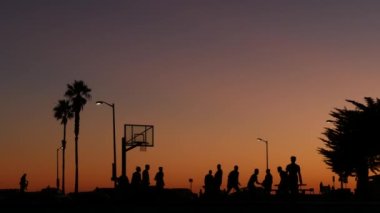 Basketbol sahasındaki insanlar basketbol oynuyor. Kaliforniya sahilinde gün batımı