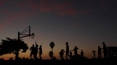 Basketbol sahasındaki insanlar basketbol oynuyor. Kaliforniya sahilinde gün batımı