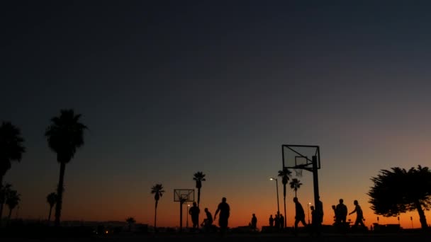 People on basketball court playing basket ball game. Sunset on beach, California — Stock Video