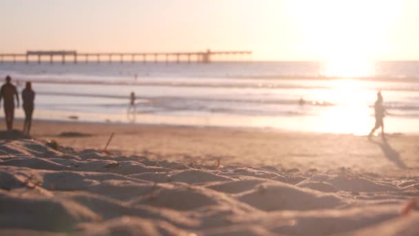 Personas caminando en la playa de arena Ocean Beach por el muelle al atardecer, costa de California, EE.UU.. — Vídeo de stock