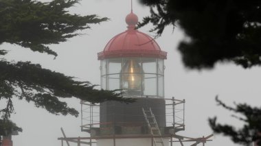 Eski deniz feneri mercekleri parlıyor, sisli yağmurlu hava. Aydınlatılmış Beacon USA