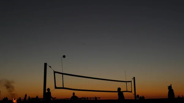 Volleyball net silhouette on beach court at sunset, players on California coast. — Stock Photo, Image