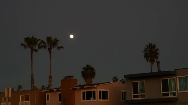 Palmeiras silhuetas e lua cheia no céu crepúsculo, Califórnia casas de praia. — Fotografia de Stock