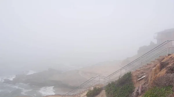 Foggy sea landscape, wave crashing on ocean beach, stairs in haze, misty weather — Stock Photo, Image