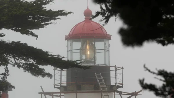 Old lighthouse fresnel lens glowing, foggy rainy weather. Illuminated beacon USA Stock Image