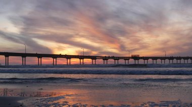 Sahildeki deniz suyunda iskele. Okyanus dalgaları, gün batımında gökyüzü. Kaliforniya kıyısı titreşimleri.
