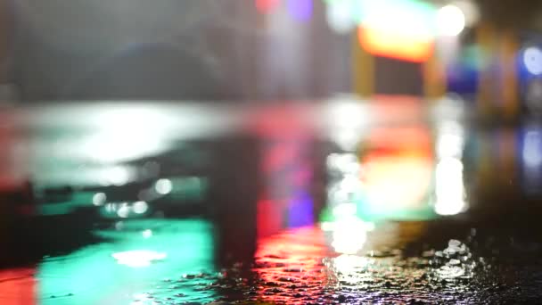 Reflexão de luzes de néon na poça na estrada. Gotas de chuva, asfalto molhado da rua da cidade — Vídeo de Stock