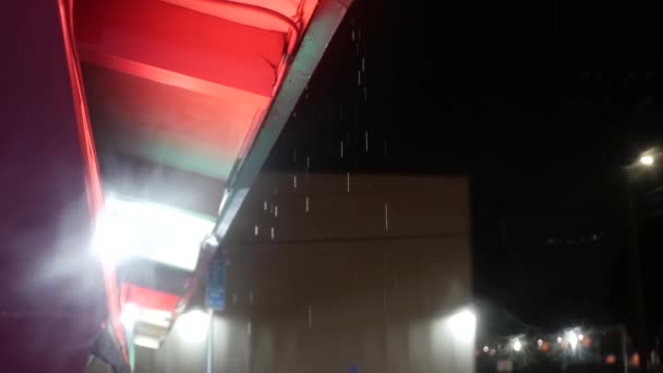 Gocce di pioggia gocciolano dal tetto. Le acque piovane gocciolano di notte. Piogge sulla strada della città. — Video Stock