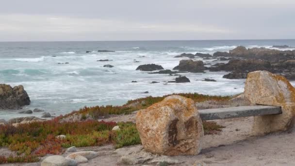 Rotsachtige grillige oceaan kust, zee golven, Monterey California. Houten lege bank. — Stockvideo