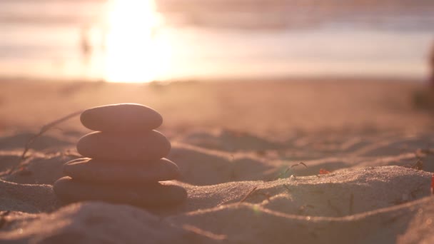 Stack of pebble stones, sandy ocean beach, sunset sky. Rock balancing by water. — Stock Video